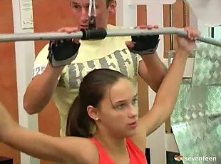 A teenage girl is working out at a gym. A guy is standing behind he...